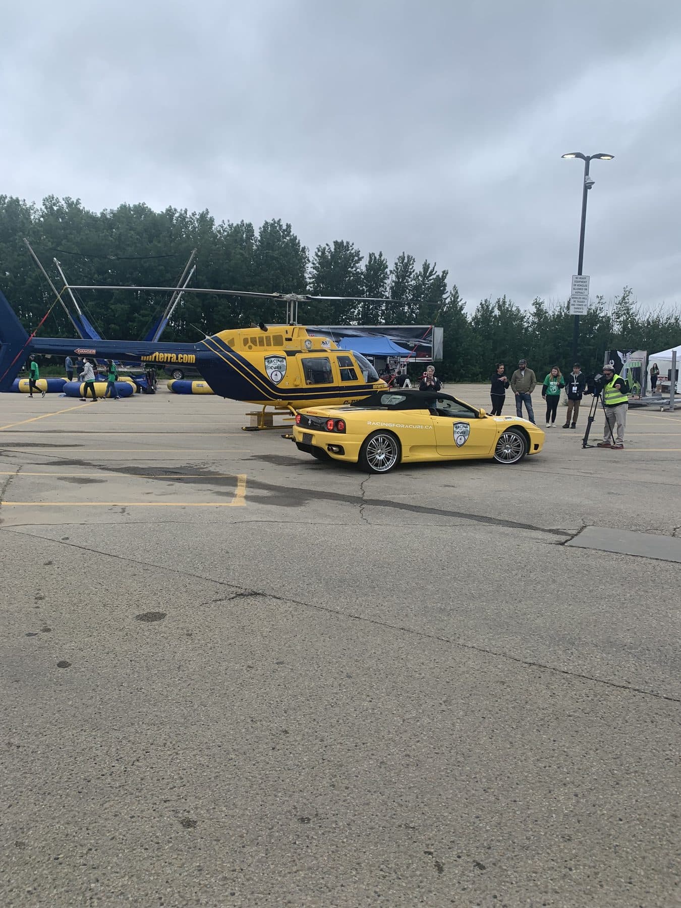 A yellow Ferrari convertible in front of a helicopter and crowd at a Racing for a Cure event.